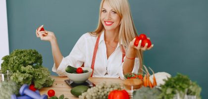Healthy lifestyle concept with woman holding tomatoes and surrounded by fresh vegetables in a studio setting.